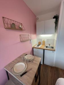 uma cozinha com paredes cor-de-rosa e uma mesa com pratos em Studio proche centre ville em Caen