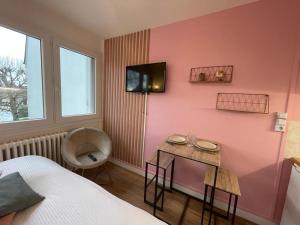um quarto com uma parede rosa com uma mesa e uma cadeira em Studio proche centre ville em Caen