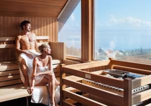 a man and a woman sitting in a sauna at Hotel Gran BelVeder & Ostsee Therme Resort & Spa in Scharbeutz