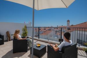 un homme et une femme assis sur un balcon avec un parasol dans l'établissement Sol da Vila, à Vila Nova de Milfontes