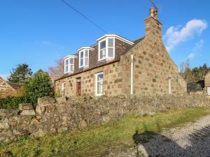 una vieja casa de piedra detrás de una pared de piedra en Wynford Holiday Cottage, en Aberdeen