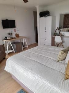 ein großes weißes Bett in einem Zimmer mit einem Schreibtisch in der Unterkunft Fijnbos Guesthouse in Knysna