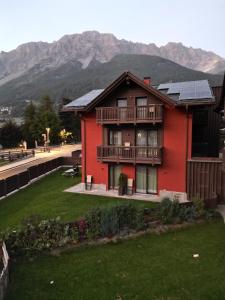 a red house with a balcony and mountains in the background at Al Bait Ross in Bormio