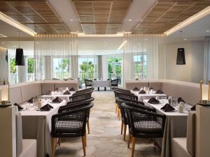 a restaurant with white tables and chairs and windows at Hilton Garden Inn Cocoa Beach-Oceanfront, FL in Cocoa Beach