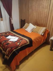 a bed with an orange blanket and white pillows at Enriqueta pds in Tolhuin