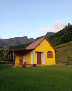 een geel en wit huis met bergen op de achtergrond bij chale 2 canto das montanhas in Caparaó Velho