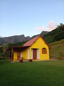 ein gelbes und weißes Haus mit Bergen im Hintergrund in der Unterkunft chale 2 canto das montanhas in Caparaó Velho