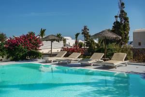 a swimming pool with lounge chairs and umbrellas at Theros Houses Santorini in Kamari