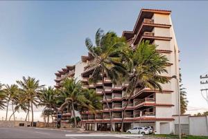 a tall building with palm trees in front of it at Flat no hotel jatiúca suítes in Maceió