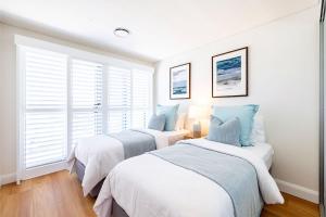 two beds in a room with white walls and windows at The Shoal, 508, Bullecourt St - stunning views, air con, lift and Wi-Fi in Shoal Bay