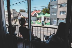 twee personen zitten op een balkon en kijken uit een raam bij Urban 1 Apartamento Bariloche in Bariloche