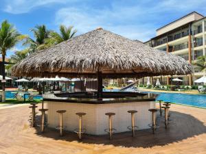 een bar met krukken onder een rieten parasol naast een zwembad bij Beach Living - Apt com 2 Quartos - Pé na Areia in Aquiraz