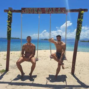 dos hombres sentados en un columpio en la playa en Cabaña privada en Guna Yala isla diablo baño compartido en Cagantupo
