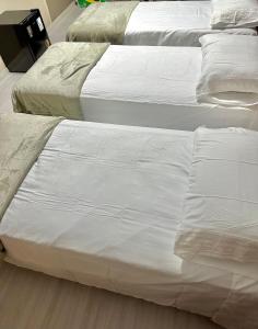 três camas brancas estão alinhadas num quarto em Loft Lux 2 em Chapecó