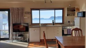 a kitchen with a table and a refrigerator and a television at Beachsider Whitianga in Whitianga
