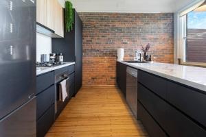 a kitchen with black cabinets and a brick wall at Launceston Stunning Outdoor Hot Tub Spa Townhouse in Invermay +8 photos