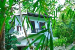 a white house with a balcony in the trees at Charming dark lodge in river in Weligama