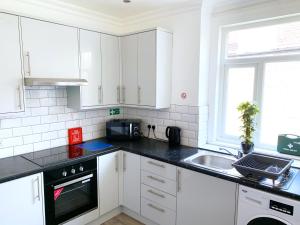 Newly Refurbished 2 Bedroom Flat - Long stays AVL في Norbury: مطبخ أبيض مع دواليب بيضاء ومغسلة