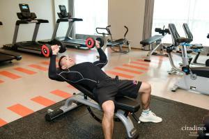 a man laying on a chair lifting weights in a gym at Citadines Keqiao Shaoxing in Shaoxing