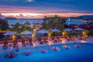 una piscina de hotel con sillas y sombrillas al atardecer en Chanalai Garden Resort, Kata Beach en Kata Beach