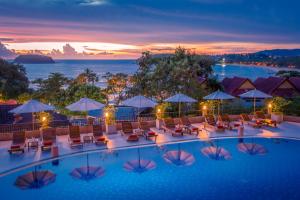 una piscina de hotel con sillas y sombrillas al atardecer en Chanalai Garden Resort, Kata Beach, en Kata Beach