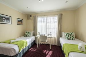 two beds in a room with a table and a window at The Henry Parkes Tenterfield in Tenterfield