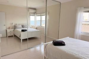 a white bedroom with a mirror and a bed at Sunny Apt on The Esplanade - Aircon in Cronulla