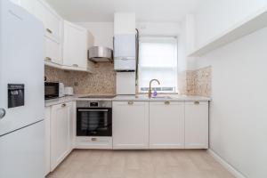 a white kitchen with white cabinets and a sink at Spacious 3BR house wbalcony, South London in London