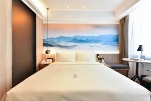 a bed in a hotel room with a painting on the wall at Atour Light Hotel Shenyang Tiexi Plaza Wanxianghui in Shenyang