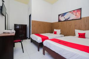 a room with two beds and a desk and a tv at RedDoorz Syariah near RSUD Tuban in Tuban