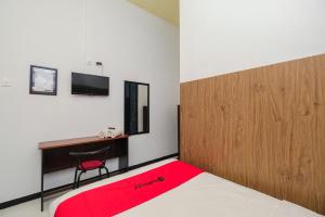 een slaapkamer met een bed en een bureau met een rode deken bij RedDoorz Syariah near RSUD Tuban in Tuban