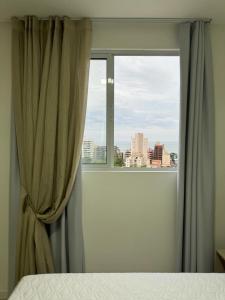 a bedroom with a window with a view of a city at Apartamento à 390m do Mar in Itapema