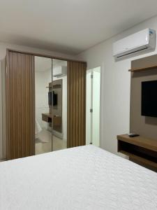 Schlafzimmer mit einem weißen Bett und einem TV in der Unterkunft Apartamento à 390m do Mar in Itapema