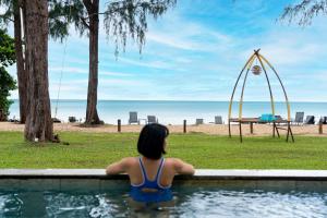 een vrouw in een zwembad die naar het strand kijkt bij Khaolak Emerald Surf Beach Resort and Spa in Khao Lak