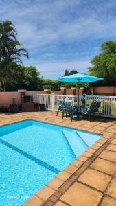 a swimming pool with two chairs and a blue umbrella at Aloe Self Catering in Port Shepstone