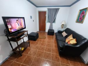 ein Wohnzimmer mit einem schwarzen Sofa und einem Flachbild-TV in der Unterkunft Departamento El Parral Parque Central in La Cieneguita