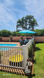 a white fence with an umbrella next to a pool at Aloe Self Catering in Port Shepstone