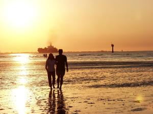 een man en vrouw die bij zonsondergang op het strand lopen bij Ferienwohnung Korte in Otterndorf