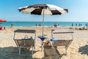 two chairs under an umbrella on a beach at Hotel Parigi in Bibione