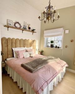 Un dormitorio con una cama grande con sábanas rosas y una lámpara de araña. en Bastuviken Bed and Breakfast en Uppsala