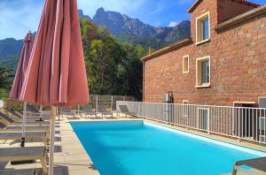 una piscina con sombrilla y sillas rojas y un edificio en Hôtel & Résidence Le Subrini, en Porto Ota