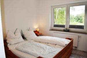 a bed with white sheets and pillows in a room with two windows at Haus Storjohann in Dagebüll