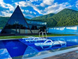 a pool with chairs and a building with mountains in the background at Qafqaz Royal Chalet in Gabala