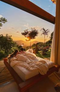 Una pareja acostada en una cama en una ventana con la puesta de sol en Cabana Canal do Infinito, en Domingos Martins