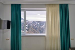 a window with green curtains and a mountain view at Hotel Lile • სასტუმრო ლილე in Khulo