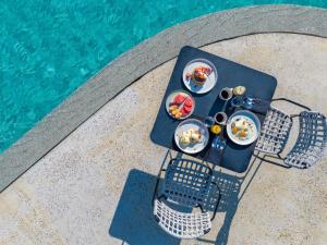 a table with plates of food next to a swimming pool at Noūs Santorini, a Member of Design Hotels in Mesaria