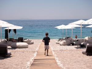 a man walking along a beach with chairs and umbrellas at La Brisa Boutique Hotel in Dhërmi