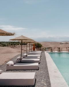 a row of lounge chairs with umbrellas next to a pool at Emeraude Camp Agafay in El Karia