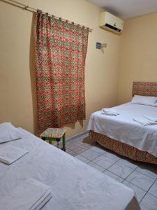 a room with two beds and a window with a curtain at Casa com ar condicionado in Lauro de Freitas