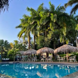 a pool with chairs and straw umbrellas and palm trees at Hotel Praia Bela in Salinópolis